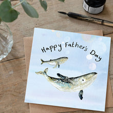 Load image into Gallery viewer, Whale and calf Father’s Day card lying on a rustic wooden table with a green plant, a pen, and an ink bottle arranged in the background.