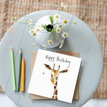 Load image into Gallery viewer, A watercolour giraffe birthday card on a wooden table alongside daisies and matching coloured pencils