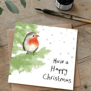Christmas card featuring robin sitting in a christmas tree laid flat on a wooden table with a matching brown envelope. 