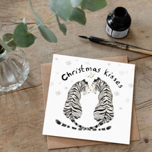 Load image into Gallery viewer, lifestyle photo of a greeting card featuring a white tiger couple smiling at each other and a text &quot;Christmas kisses&quot; above them