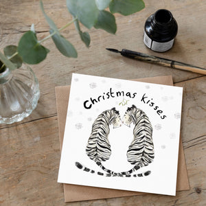 lifestyle photo of a greeting card featuring a white tiger couple smiling at each other and a text "Christmas kisses" above them