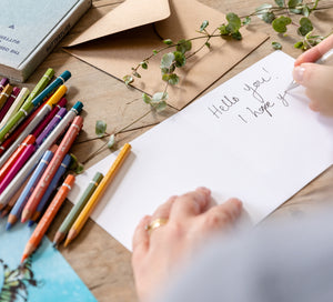 Catherine handwriting a personalised messaged in a card, surrounded by art supplies.