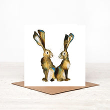 Load image into Gallery viewer, A white square greetings card featuring a watercolour illustration of two hares,  stood up on a matching brown craft envelope.