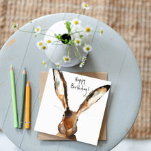 Load image into Gallery viewer, Watercolour hare birthday card lying on wooden table with daisies and matching coloured pencils