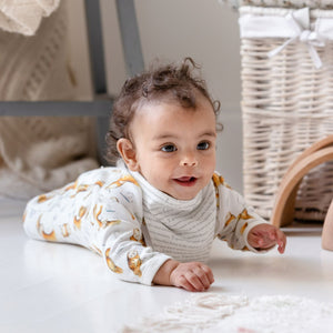 six month old baby wearing the bib with the story printed side facing out, and an olive owl babygrow. She is crawling towards us, smiling