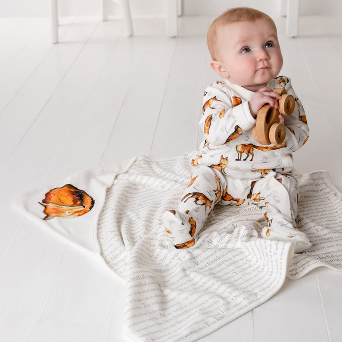 Six month old baby sitting up, wearing dexter fox print babygrow and sitting on dexter fox print blanket.